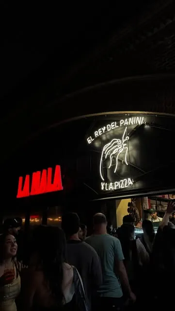 El cartel de neón de El Rey Del Panini de noche en La Mala, con gente en la puerta