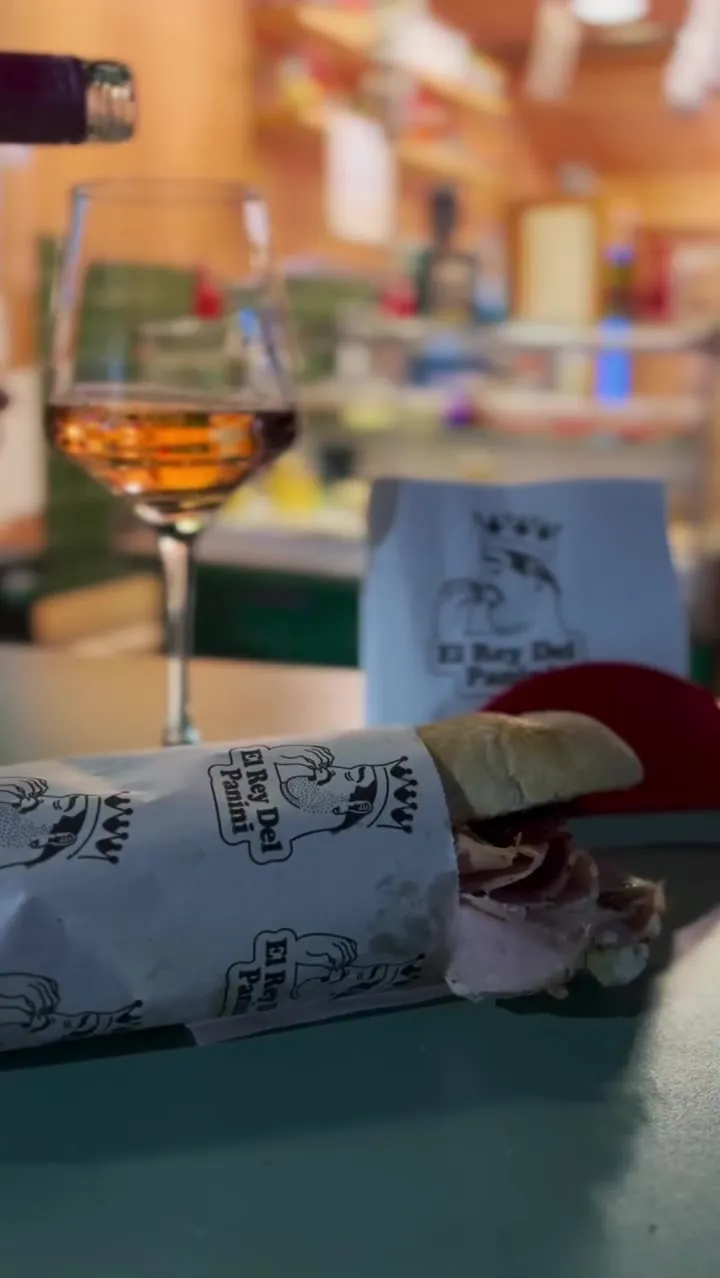 Copa de vino junto a un panini envuelto en el papel de la casa